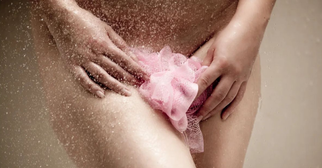 Mujer en la ducha usando una esponja rosa para higiene íntima, representando el uso adecuado de espuma limpiadora para mantener el pH balanceado.